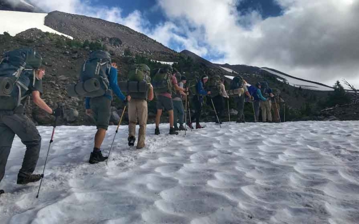 a group of outward bound students carrying backpacks hike across a snowy field on an expedition in oregon